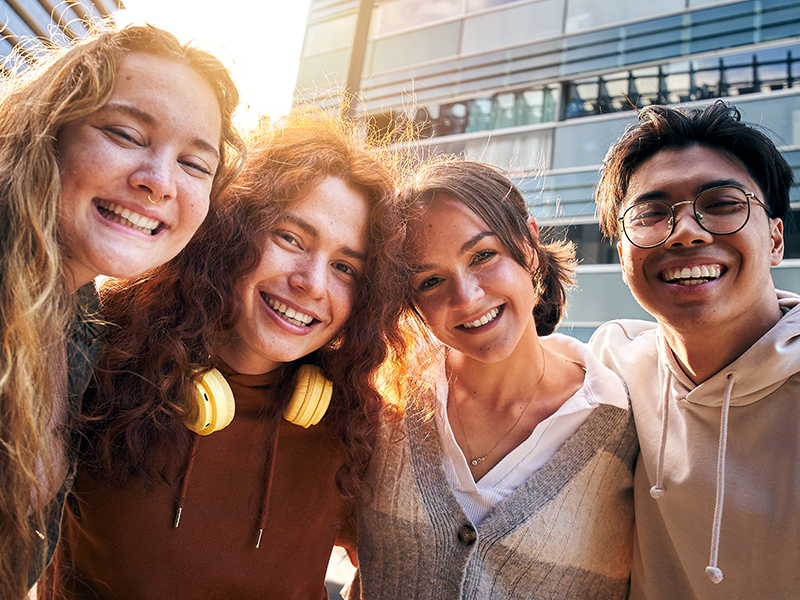 Erasmus International university students looking at camera happily hugging each other outdoors.